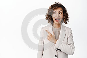 Smiling enthusiastic businesswoman pointing left, looking at logo advertisement with happy face expression, showing