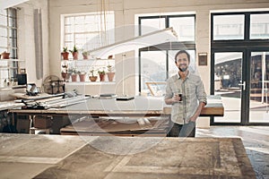 Smiling entrepreneur standing in his workshop with coffee