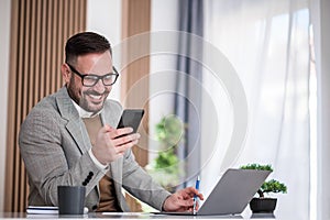 Smiling entrepreneur taking a phone call in his home office creative young man using laptop computer and smart phone freelancer