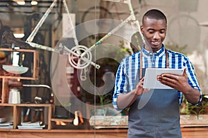 Smiling entrepreneur using a tablet in front of his cafe