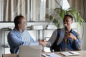 Smiling ethnic male colleagues handshake at office meeting