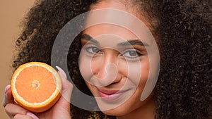 Smiling ethnic model girl African American woman hold half healthy orange fruit shake head with curly hair curls
