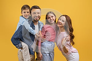 Smiling European Family of Four Posing Together Against Yellow Background