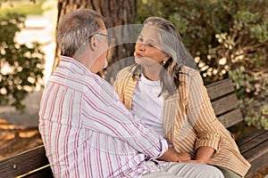 Smiling european mature couple sit on bench, enjoy date together in park, want to kiss at weekend