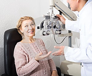 Mature optician examinating eyesight with aid of slit lamp