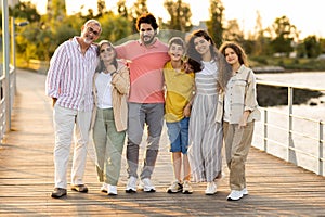 Smiling european multi-generation family hugs, enjoy vacation in city park, walk outdoor, full length
