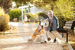 Smiling european old man in casual and glasses enjoy walk with dog and spare time, hugs in park, outdoor