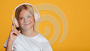 Smiling european teen girl in white t-shirt and wireless headphones listening music or lesson online