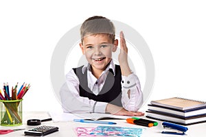 Smiling excellent pupil with hand up sitting at the table on the white background