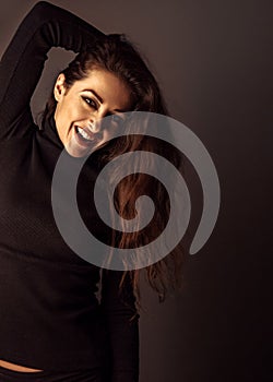 Smiling excited beautiful woman. Female with brown long hair posing on dark shadow background.