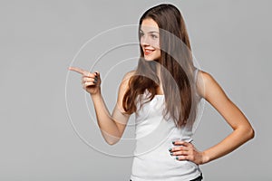 Smiling excited woman showing finger on copy space for product or text, on gray background