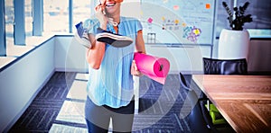 Smiling executive talking on mobile phone while holding exercise mat and shoes