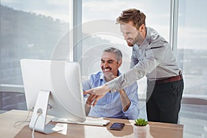 Smiling executives discussing over personal computer at desk