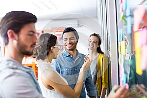 Smiling executives discussing over sticky note on glass wall