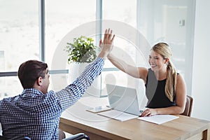 Smiling executives giving high-five to each other at desk