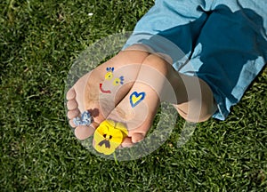 Smiling face and heart painted on child bare feet in yellow and blue