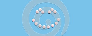 Smiling face lined with pink pills on a blue background