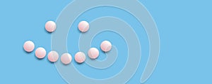 Smiling face lined with pink pills on a blue background, top view