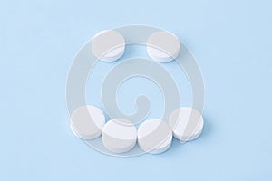 Smiling face made from white round pills on blue background. Medicine and health care concept. Top view
