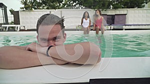 Smiling face of wet young guy getted out from the open-air swimming pool on the background of two beautiful girls. A