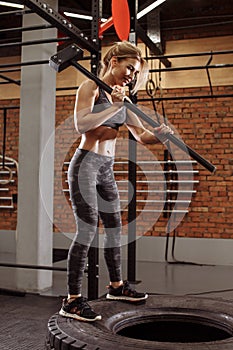 Smiling fair-haired girl standing on the huge tire with sledgehammer