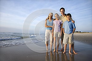 Portrét Kaukazských rodiny štyri pózuje na pláži pri pohľade na diváka s úsmevom.
