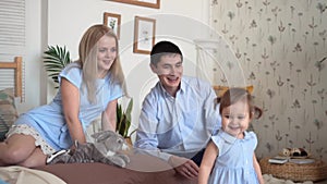 Smiling family in bed where dad and mom play with their little daughter.