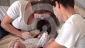 Smiling family in bed where dad and mom are watching, touching and talking with their baby daughter.