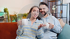 Smiling family couple man woman drinking a cup of coffee or herbal tea at home couch in the morning