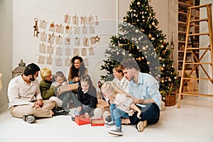 Smiling family exchanging and opening gifts while sitting near Christmas tree