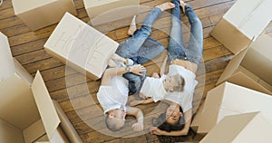 Smiling family of four lying on the floor, view from the top. young family moving to a new apartment and carrying boxes