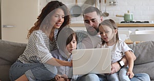 Smiling family of four using laptop, shopping at home.