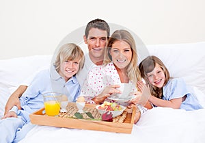 Smiling family having breakfast sitting on bed