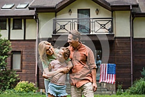 Smiling family hugging daughter near blurred