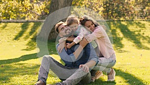 Smiling family hugging each other, while sitting on green field