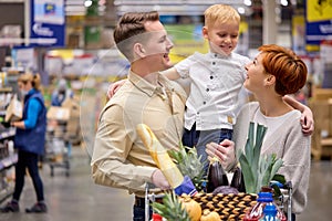Smiling family hugging, smiling, in love while shopping in supermarket standing In store aisles indoors