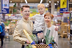 Smiling family hugging, smiling, in love while shopping in supermarket standing In store aisles indoors