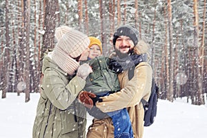 Smiling family hugging son and looking at the camera under snowfall in the forest