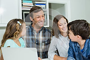 Smiling family interacting with each other while using laptop in living room