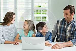 Smiling family interacting with each other while using laptop in living room