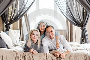 Smiling family lie on a white bed