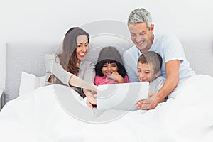 Smiling family lying in bed using their laptop