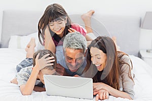 Smiling family lying on bed using their laptop