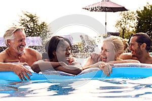 Smiling Family With Mature Parents And Adult Offspring On Summer Holiday In Swimming Pool On Airbed