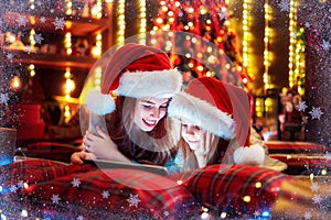 Smiling family mother and daughter in santas hats and pajamas watching funny video or choosing gifts on digital tablet