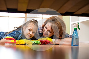 Smiling family mother and her daughter clean room at home. Middle-aged woman and child girl wiped floor under bed