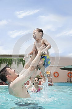 Smiling family playing in the pool, father lifting his son out of the water