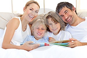 Smiling family reading a book on bed