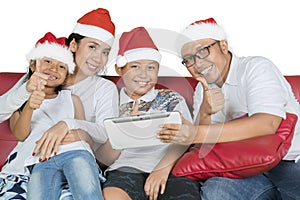 Smiling family with thumbs and tablet at Christmas