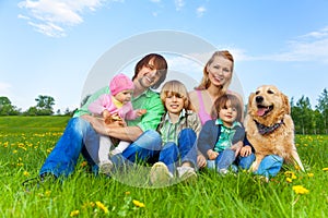 Smiling family sitting on green grass with dog